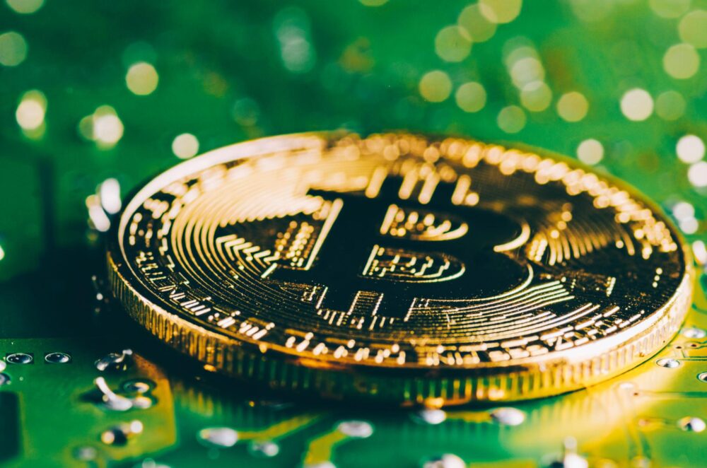 Golden Bitcoin cryptocurrency coin on a green circuit board representing blockchain technology and digital finance.